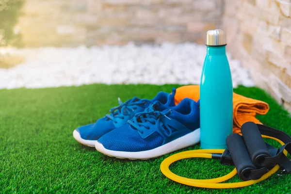 Close-up of objects and accessories for practising sport in a green grass garden. rubber bands for stretching, towel, water bottle. concept of practising sport in the open air. natural outdoor light.