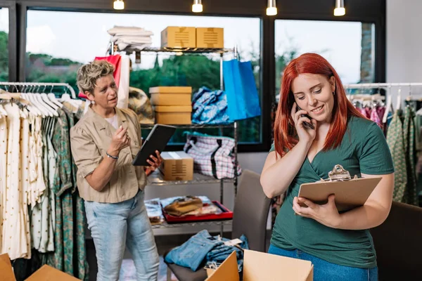 coworkers, working in the warehouse of the clothing shop, receiving calls from their customers and suppliers. mature businesswoman and young employee. business concept and entrepreneur. natural light