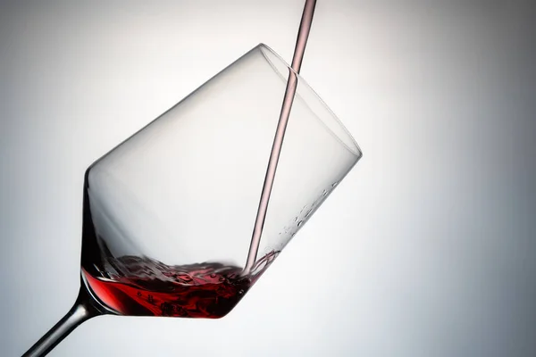 close-up of filling a crystal glass with red wine. pouring red wine into a crystal glass isolated on a grey background. image to cut out. concept drinks. Hard ligth