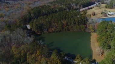 Ağaçlarla çevrili üçgen gölün sağından soluna doğru tam hava drone çember görüntüsü