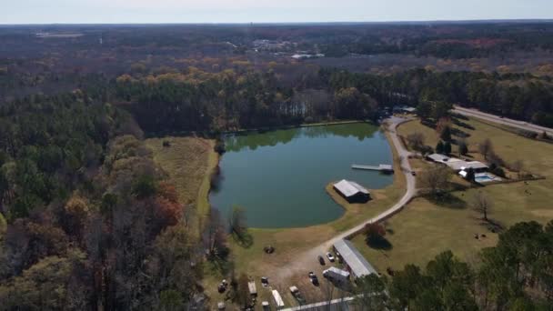 Mosca aérea para lago em forma ímpar verde com estrada e árvores celeiro ao lado do lago — Vídeo de Stock