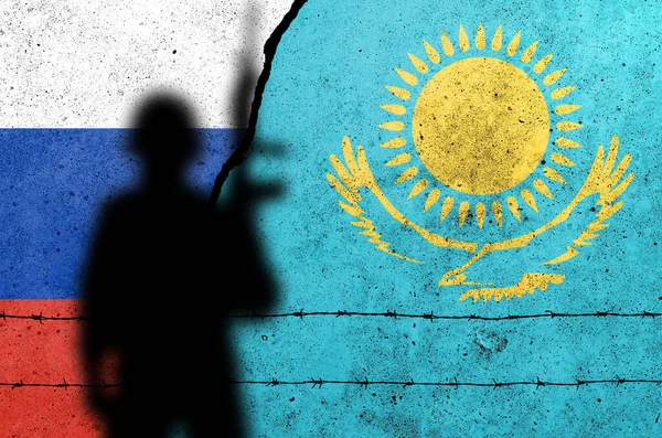 Russia and Kazakhstan flags painted on a concrete wall with soldier shadow. Relationship between Kazakhstan  and Russia