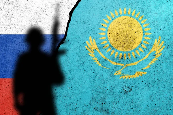Russia and Kazakhstan flags painted on a concrete wall with soldier shadow. Relationship between Kazakhstan  and Russia