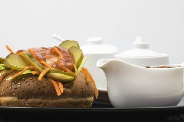 Havuç, sos ve salatalıklı yuvarlak bir ekmeğin üzerinde iştah açıcı sosis.