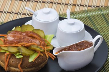 Havuçlu, soslu ve salatalıklı yuvarlak ekmeğin üzerinde iştah açıcı sosis.