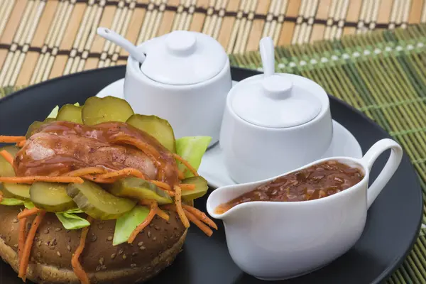 Havuçlu, soslu ve salatalıklı yuvarlak ekmeğin üzerinde iştah açıcı sosis.