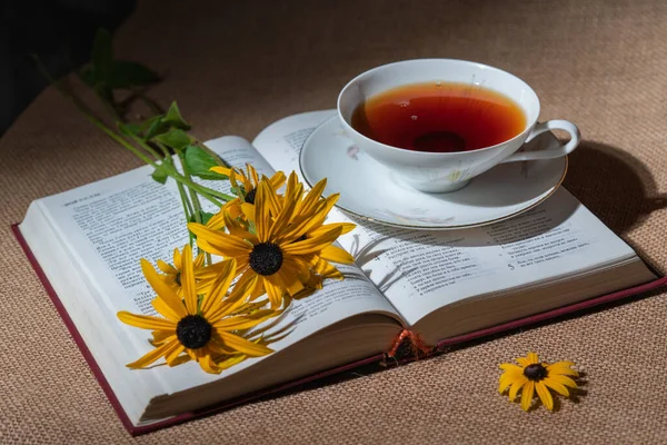 Çiçeklerle dolu açık bir kitap ve masada bir fincan çay.