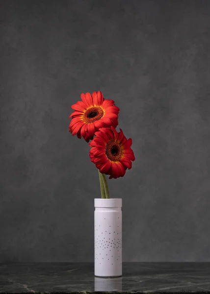 Two red flowers in a white vase on a green marble table. Love and understanding. Together forever. Warm, joyful relationships. Feeling each other next to each other. Pleasure.