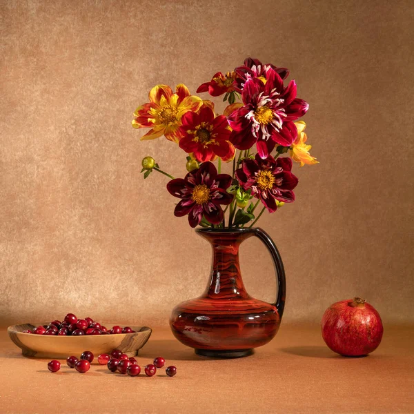 A bright bouquet of flowers in a clay jug. Fruits and berries on the table. Pomegranate and cranberry. Orange background. Healthy foods. Vegan. The taste and smell of autumn. Pleasant aroma. Tranquility