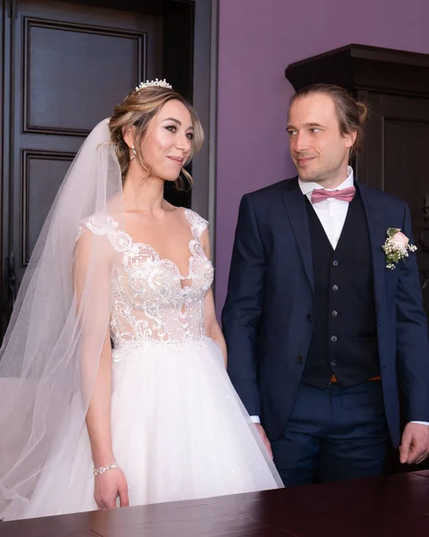 Marriage. Young bride and groom in a white wedding dress and blue suit. Wedding and engagement rings. A couple of newlyweds. Pledge of fidelity and love. Solemn event in people's lives