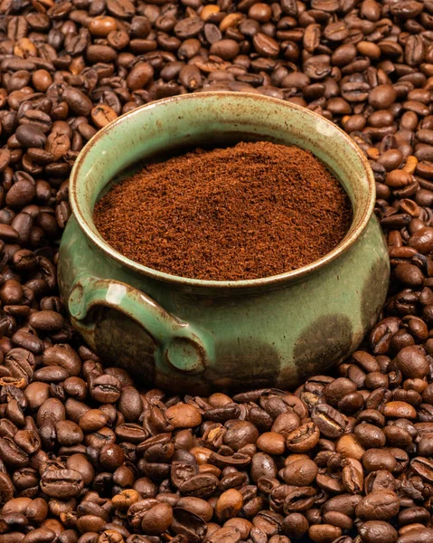 A green earthenware cup with ground coffee in the middle of many coffee beans. Diversity. Taste difference. Cheerfulness. Awakening. Tonic drink. Aroma of coffee. Breakfast. Choice. Energy of the day