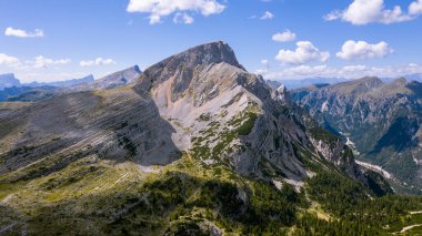 Yüksek kayalar. İtalya 'da Alpler. Güney Tyrol. Dolomitler. Taşları ve yeşil bitkileri olan yeşil bir arazi. Dağ manzarası. İHA 'dan ateş ediliyor. Bir helikopterden fotoğraf. Turizm. Mavi bulutlar.