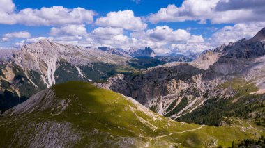 Yüksek kayalar. İtalya 'da Alpler. Güney Tyrol. Dolomitler. Taşları ve yeşil bitkileri olan yeşil bir arazi. Dağ manzarası. İHA 'dan ateş ediliyor. Bir helikopterden fotoğraf. Turizm. Mavi bulutlar.