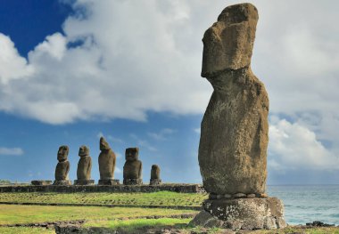 Moai heykellerinin yakın görüntüsü mavi gökyüzünde bulutlar ve Pasifik Okyanusu arka planında. Paskalya Adası, Şili (Rapa Nui)