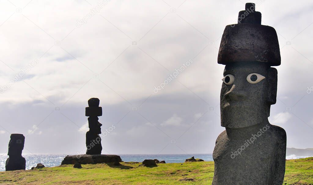 Three Moai statues of Ahu Tongariki on a cloudy sky, green grass and Pacific ocean background. Easter Island (Rapa Nui), Chile