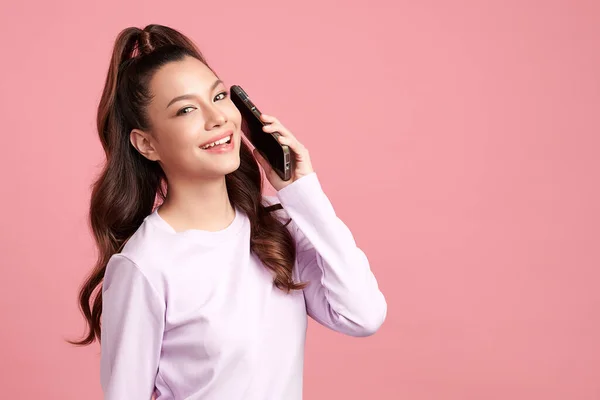ピンクの背景にオンラインパートナーとチャットスマートフォンで笑顔の美しい若いアジアの女性 — ストック写真