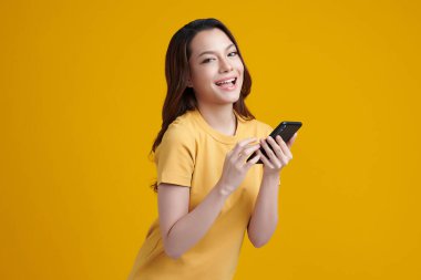 Zeki telefonuyla gülümseyen güzel Asyalı kadınlar sarı arka planda partnerleriyle sohbet ediyorlar.,