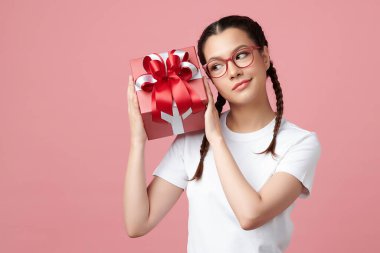 Şirin Asyalı kız hediye kutusunu tutuyor ve pembe arka planda duruyor. Reklam içeriğiniz için boş fotokopi alanı..
