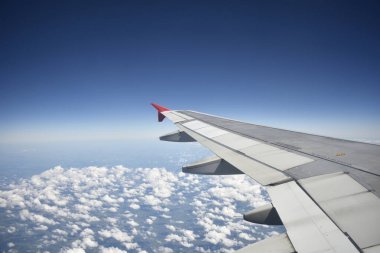 Açık bir günde, beyaz bulutların üzerinde mavi gökyüzünü geçen bir uçağın penceresinden bakmak.