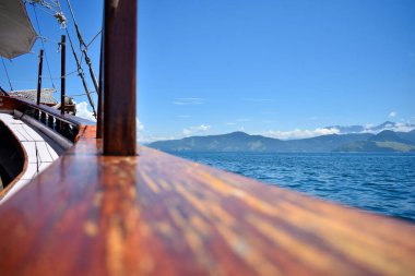 Denizle çevrili ahşap teknenin pruvasını ve ufukta kaybolmuş dağların ve bulutların kıyılarını görebileceğiniz bir yelkenlinin manzarası.