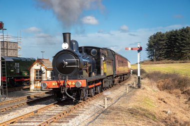 Kuzey Norfolk, İngiltere 'deki Weybourne' daki Poppy Line istasyonuna mavi gökyüzü gününde buharlı tren yaklaşıyor.