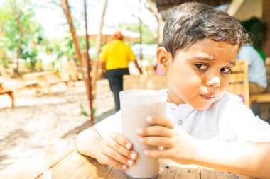 Latin çocuk elinde bir bardak geleneksel sütlü çikolata içeceği tutuyor, adı kakao. Garson servis yaptıktan sonra yürüyüp gidiyor.