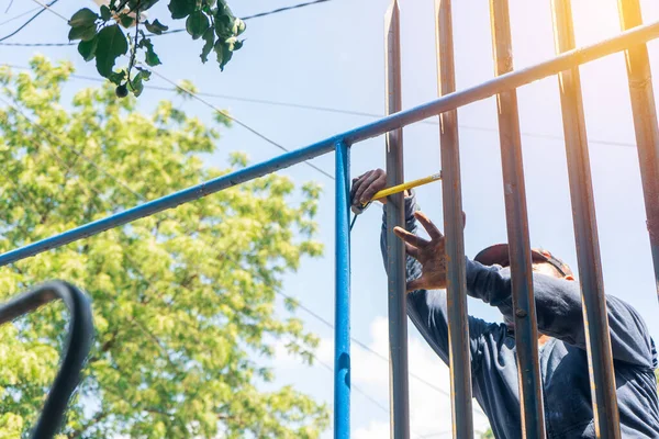 Trabajador de cuello azul al aire libre midiendo varillas de acero mientras instala una valla metálica. — Foto de Stock
