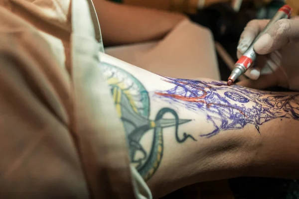 Zbliżenie ręki latynoskiego tatuażysty oznaczające szkic tatuażu na męskiej nodze markerem. — Zdjęcie stockowe