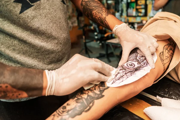 Zbliżenie Latynoskiego tatuażysty w rękawiczkach medycznych, robiącego szkic tatuażu na nodze swoich klientów w swoim studio w Managua — Zdjęcie stockowe