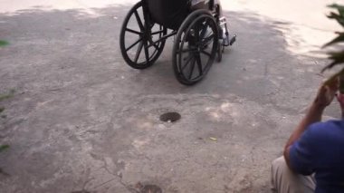 İnsanlar yanından geçerken tekerlekli sandalyesinde oturan engelli.
