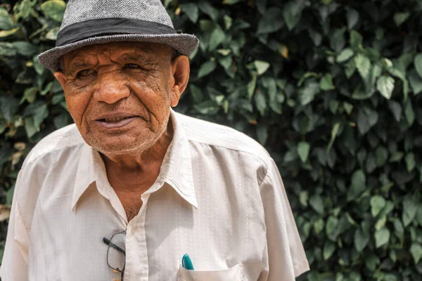 Jinotega Nikaragua 'da arka planda bitkilerle kameraya bakan şapkalı emekli Latin adam.