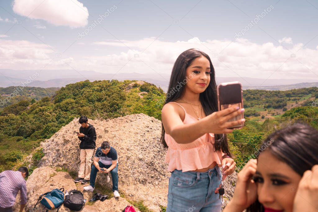 Teenagers enjoying, resting and taking photos with their cell phones on top of a mountain in Jinotega, Nicaragua