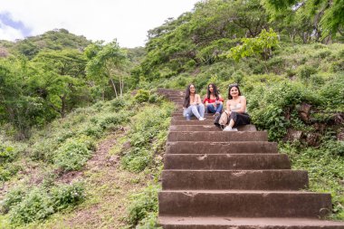 Latin gençler okul gezisinde dağ başında beton basamaklarda oturuyorlar.