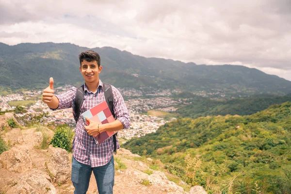 Latin college student with thumb up outdoors in mountain