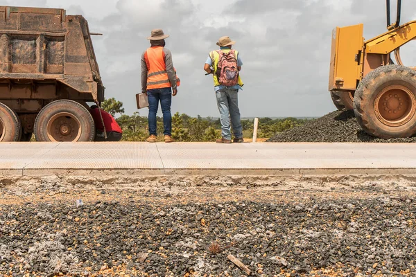 Two Latino blue collar workers supervising the construction of a hydraulic concrete road in Nicaragua