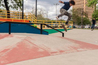 Latino teenager jumping with his skateboard in a park outdoors in Latin America