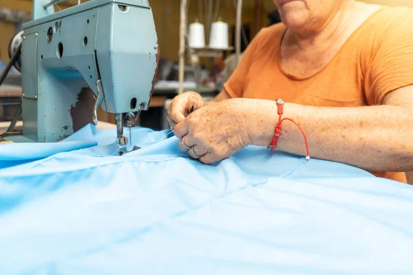 Aktif yaşlı bir kadın dikiş makinesine Guayabera gömleği dikiyor.