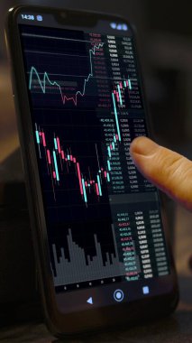 Bir adamın parmağı Android akıllı telefonunun dokunmatik ekranında çeşitli borsa grafikleri var.