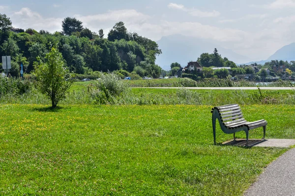 Yeşillik bir parkta, arkasında dağlar olan bir bank.