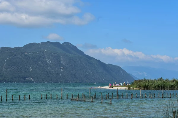 İnsanlar Fransız Alplerinde bir gölün kıyısında kumsalın keyfini çıkarıyorlar.