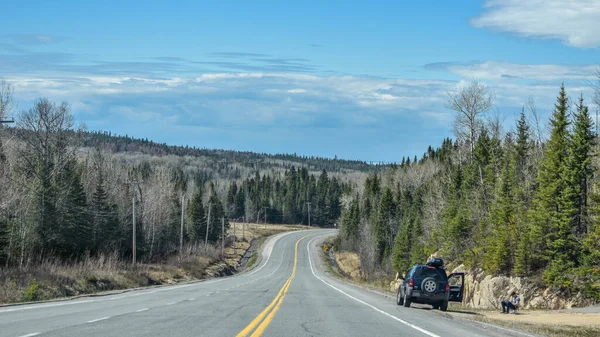 Yol kenarında bir insan ve arabayla ormanı geçen bir yolun manzarası. Quebec, Kanada