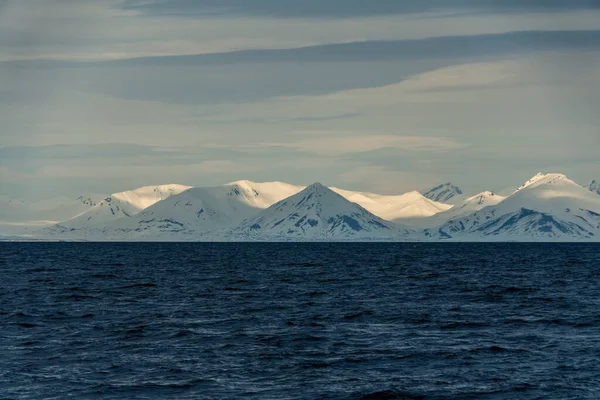Norveç, Svalbard 'da dağların mavi saatinin panoramik manzarası, kar ve deniz.
