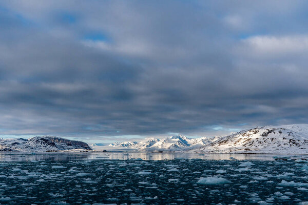 Sea with melting ice cubes, snowy mountains In Svalbard, Norway. Global Warming.