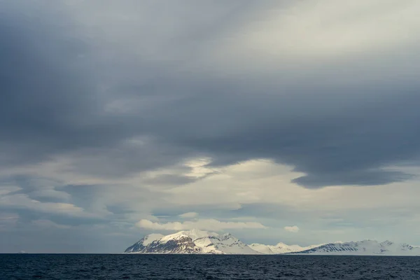 Norveç, Svalbard 'da dağların mavi saatinin panoramik manzarası, kar ve deniz.