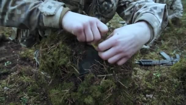 Soldier make a camouflage for a helmet. In pine forest. Preparing for the attack — Stock Video