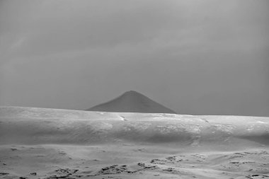 Mavi saatin panoramik görüntüsü. Svalbard takımadalarının manzarası, deniz, dağlar ve dramatik gökyüzü. Karanlık sakin deniz, karla kaplı dağlar ve karanlık gökyüzü siyah beyaz fotoğraf Küresel Isınma.