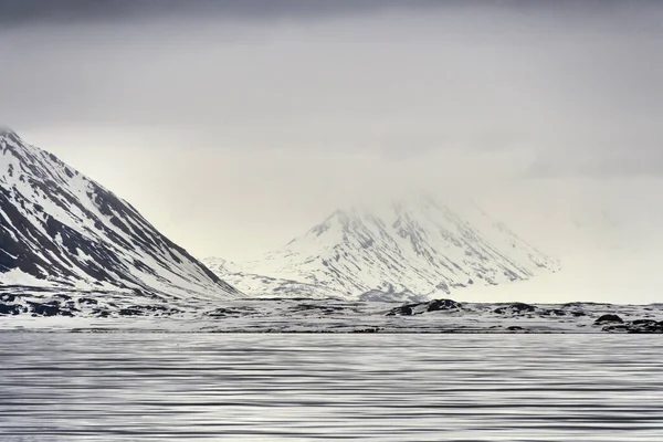Mavi saatin panoramik görüntüsü. Svalbard takımadalarının manzarası, deniz, dağlar ve dramatik gökyüzü. Karanlık sakin deniz, karla kaplı dağlar ve karanlık gökyüzü. Yüksek kalite fotoğraf