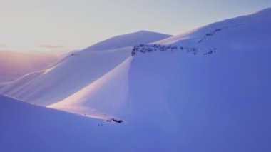 Longyearbyen yakınlarında insansız hava aracı Svalbard 'daki karlı dağların ardında batıyor. Uçuşlar uçurum ve beyaz karlı dağlar boyunca yüksek kaliteli 4K görüntüler