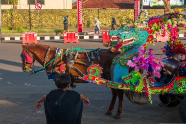 Kuningan, Endonezya - 17 Mart 2022: Kuningan, Batı Java 'da güneşli bir öğleden sonra, arka planda binalar bulunan renkli bir at arabası