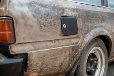 İhmal edilmiş eski bir araba yeni bir benzin deposu kapağıyla çelişiyor.. 